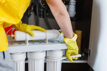 Plumber in yellow household gloves changes water filters. Repairman changing water filter...