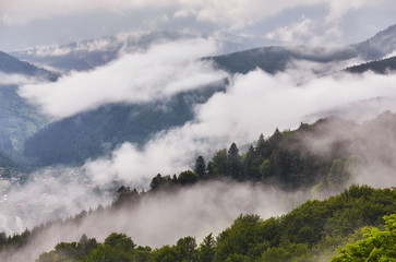 Summer mountain panorama. Small wooden house cottage and barn on green mountain valley on bright foggy sky, clouds and mountain