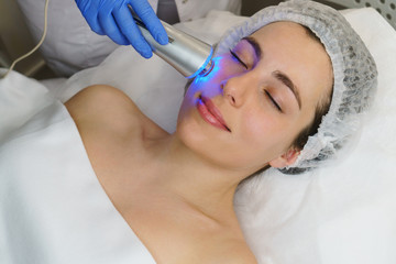 Hardware cosmetology. Ultrasound chromotherapy. Beautician carries out procedure for tightening skin of face. Spa. Non-surgical cosmetology. Skin elasticity
