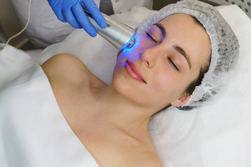 Naklejka premium Hardware cosmetology. Ultrasound chromotherapy. Beautician carries out procedure for tightening skin of face. Spa. Non-surgical cosmetology. Skin elasticity