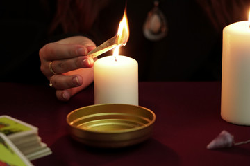 Witch is fortune teller in black mantle make magical rite and burns spell. Tarot cards, amethyst stone, white candles on dark mystic background. Occult, esoteric, divination and wicca concept.