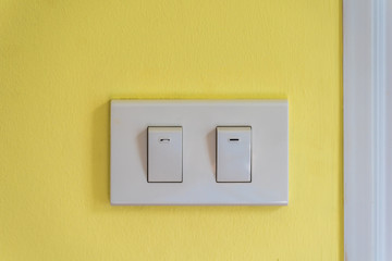Two white lighting switchs on yellow concrete wall