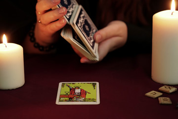 A witch is fortune teller in a black robe mixes a tarot deck.Tarot cards, ancient runes and white candles. Occult, esoteric, divination and wicca concept. Mystic and vintage background.