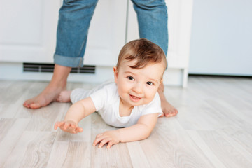 Charming little boy 6 months smiling and looking at the camera on the background of mom's feet