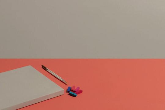 Lienzo en blanco con pinceles y tizas de acuarela en colores azules y rosas sobre un escritorio color coral y pared gris