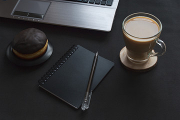 Office desk with coffee and donut on a black background. Snack at work
