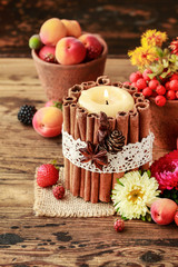 Candle decorated with cinnamon sticks among autumn fruits and flowers.