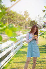 Asian woman send sms on cellphone in park. Happy female  speak and use smart phone outdoor.