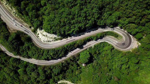 Aerial fly under curved winding road trough the mountains