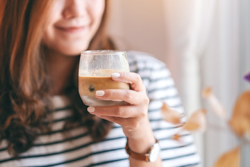 Closeup image of a beautiful woman holding a glass of iced coffee to drink in cafe