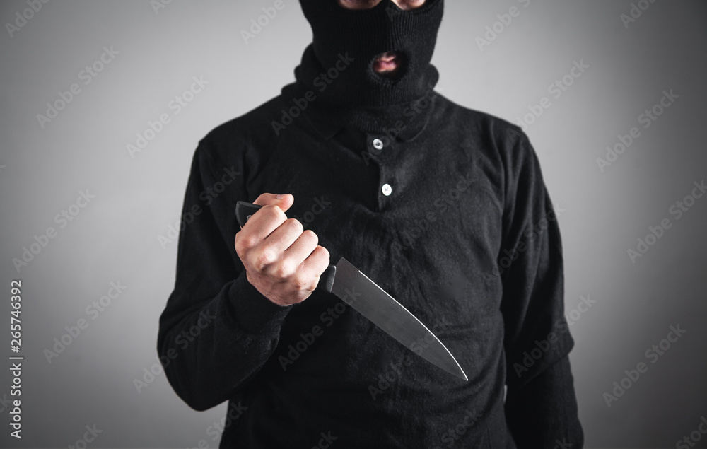 Wall mural killer in black mask threatening with knife. crime and robbery concept