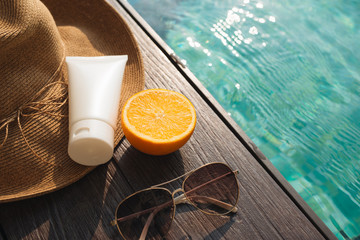 Orange juice, straw hat, sunblock and sunglasses by poolside