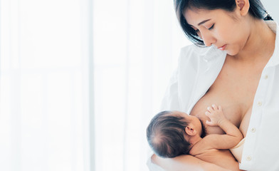 Asian newborn baby with mother concept : young mother breast feeds newborn in living room