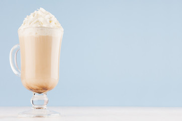 Refreshment morning cappuccino coffee with whipped cream in exquisite transparent glass with handle in light blue interior, copy space.