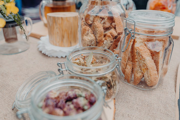 Linden flowers in glass jar on the table, jars with red clever and cookies near. Horizontal orientation.