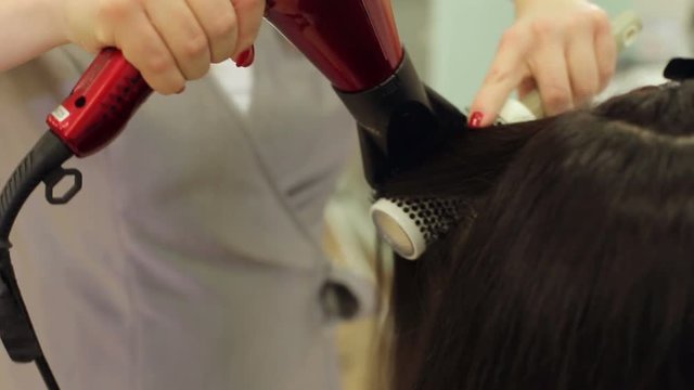 Close-up of the process of hair styling in a beauty salon with a hair dryer and a comb. The hairdresser dries the girls wet hair with a hair dryer and combs the comb.