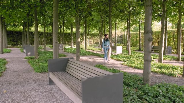 Hannover, Germany. A young female tourist with a map in her hands and a backpack walks along the avenues of the park. Opens a paper map and looks the way in it. In the frame a lot of trees and stone