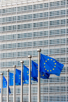 A row of european flags blowing in the wind at full-mast in front of the Berlaymont building, headquarters of the European Commission, the executive of the European Union (EU) in Brussels, Belgium.