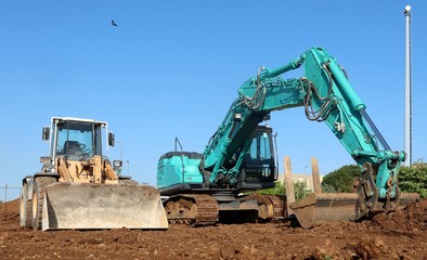 A green excavator flanked by a bulldozer on the dirt of the newly opened construction site