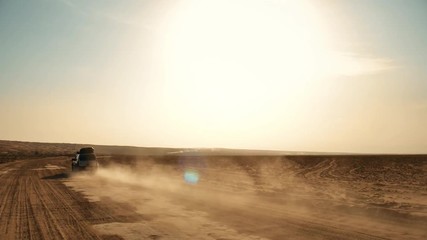 Following shot of a moving off-road 4WD silver car on desert and dust trail A big muscle 4WD offroad car driving alone on sandy way middle of wide desert and dust and sands flow under natural sunlight