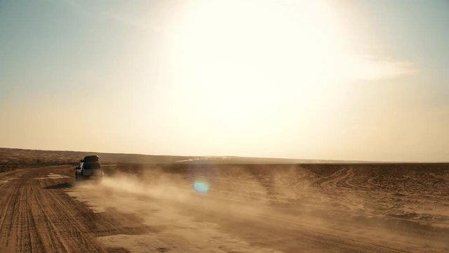 Following shot of a moving off-road 4WD silver car on desert and dust trail A big muscle 4WD offroad car driving alone on sandy way middle of wide desert and dust and sands flow under natural sunlight