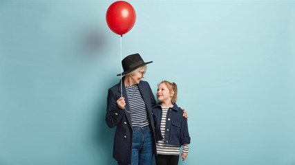 Old grandmother and small child have nice conversation, hold red air balloon, express love to each...