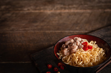 Instant noodle with pork, egg and vegetables on black bowl on the wood table there are chilli and chopstick placed around.