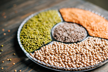 Various legumes red lentils, mung beans and chickpeas in a glass plate on a wooden table close up