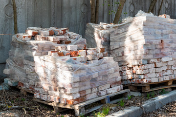 Old bricks stacked on a wooden frame partially covered with polyethylene.