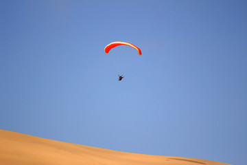 Fototapeta na wymiar the sport of jumping from the sand dune and performing acrobatic maneuvers in the air during free fall before landing by parachute