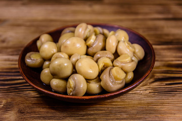 Ceramic plate with canned mushrooms on wooden table