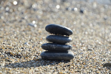 Fototapeta na wymiar Zen pyramid of spa stones on the blurred sea background. Sand on a beach. Sea shores. Water waves texture. Place for text. concept of balance and spirituality