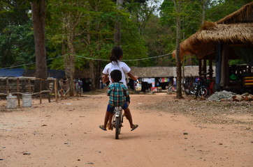 カンボジアのシェムリアップ　世界遺産のアンコールワット遺跡群　遺跡内の住居とお店　自転車に乗るカンボジアの姉弟