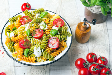Italian food - Salad with colorful pasta, cherry tomatoes, feta cheese and fresh basil on white wooden background