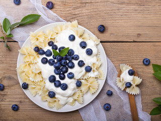 Tasty pasta with fresh organic blueberries and vanilla cream. Sweet dinner on retro wooden table.