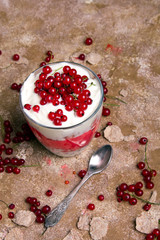 Healthy dessert with organic red currants, fresh yogurt and corn flakes. Dietary breakfast on a brown background