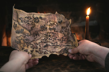 Adventurer man is holding in hands a treasure map over a burning fire background. Treasure hunt...