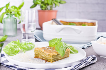 Traditional Italian cuisine for lunch. Lasagna with pesto and basil in a porcillo plate. White dishes on the table.
