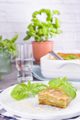 Traditional Italian cuisine for lunch. Lasagna with pesto and basil in a porcillo plate. White dishes on the table.