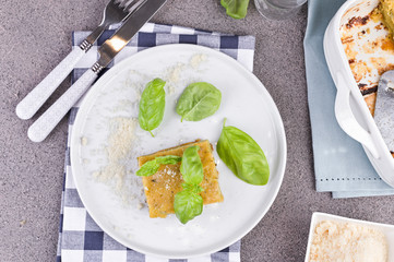 Traditional Italian cuisine for lunch. Lasagna with pesto and basil. White dishes on the table.Copy space