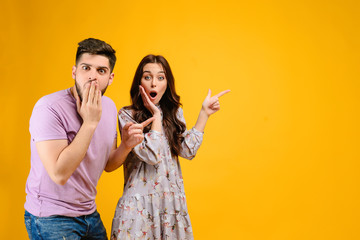Photo of young couple man and woman surprised pointing at copy space  isolated over yellow...