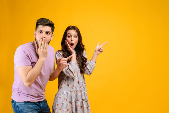 Photo Of Young Couple Man And Woman Surprised Pointing At Copy Space  Isolated Over Yellow Background