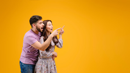 Attractive young couple of man and woman pointing at copy space isolated over yellow background