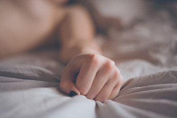 Hand sign orgasm of woman on white bed. Hand of female pulling white sheets in ecstasy. Feeling and emotion concept. Love sex concept. - obrazy, fototapety, plakaty