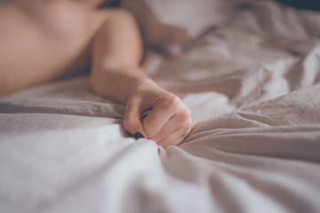 Hand sign orgasm of woman on white bed. Hand of female pulling white sheets in ecstasy. Feeling and emotion concept. Love sex concept. - obrazy, fototapety, plakaty