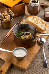 Thick forest mushroom soup with potatoes and sour cream in pot on wooden table