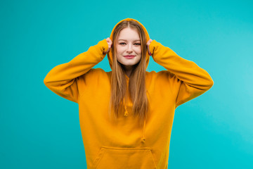 Portrait of a young emotional woman in a yellow hoodie isolated over blue background