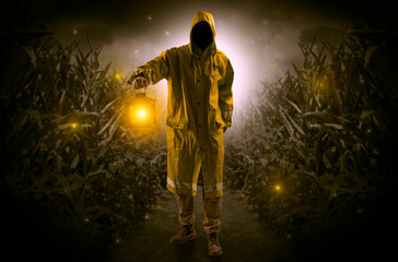 Man in raincoat at night coming from thicket and looking something with glowing lantern
