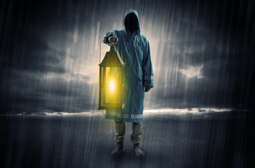 Raincoated man walking in storm with glowing lantern in his hand
