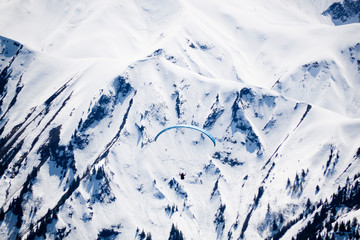 one blue parachute flying in the sky over snowed mountains